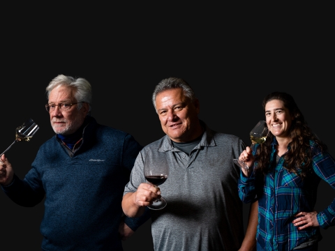 three people posing with glasses of wine featured in front of a black background